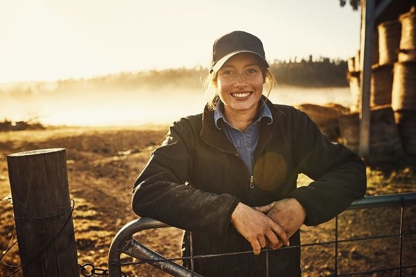 Portrait of a young woman leaning against a gate on a farm